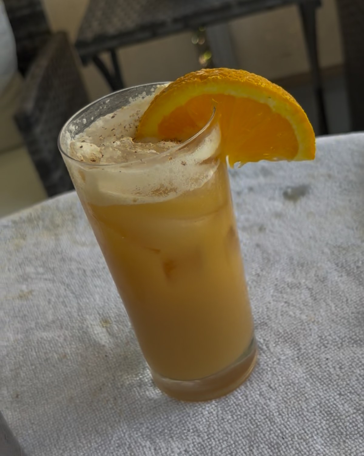 Orange cocktail dusted with fresh nutmeg and finished with an orange wedge.
